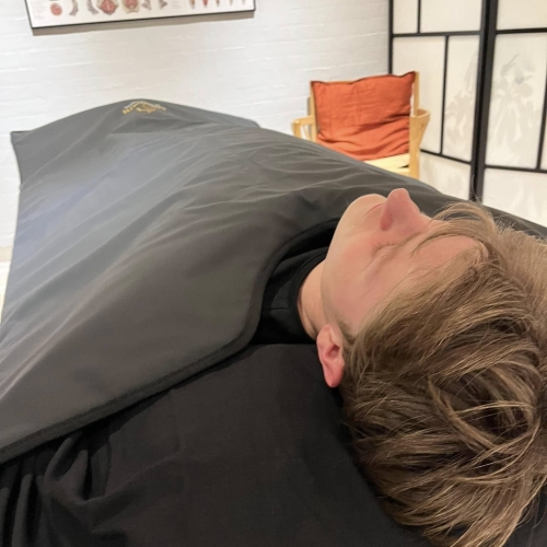 Klient i varmetæppe under afslapning i forbindelse med massage hos Klinik MasAku i Odense