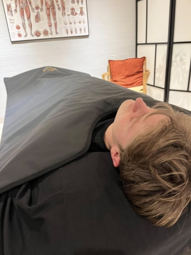 Klient i varmetæppe under afslapning i forbindelse med massage hos Klinik MasAku i Odense
