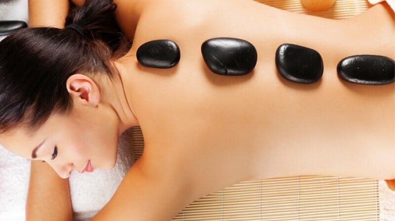 Hot stone massage på kvindes ryg som del af wellnessbehandling i Odense
